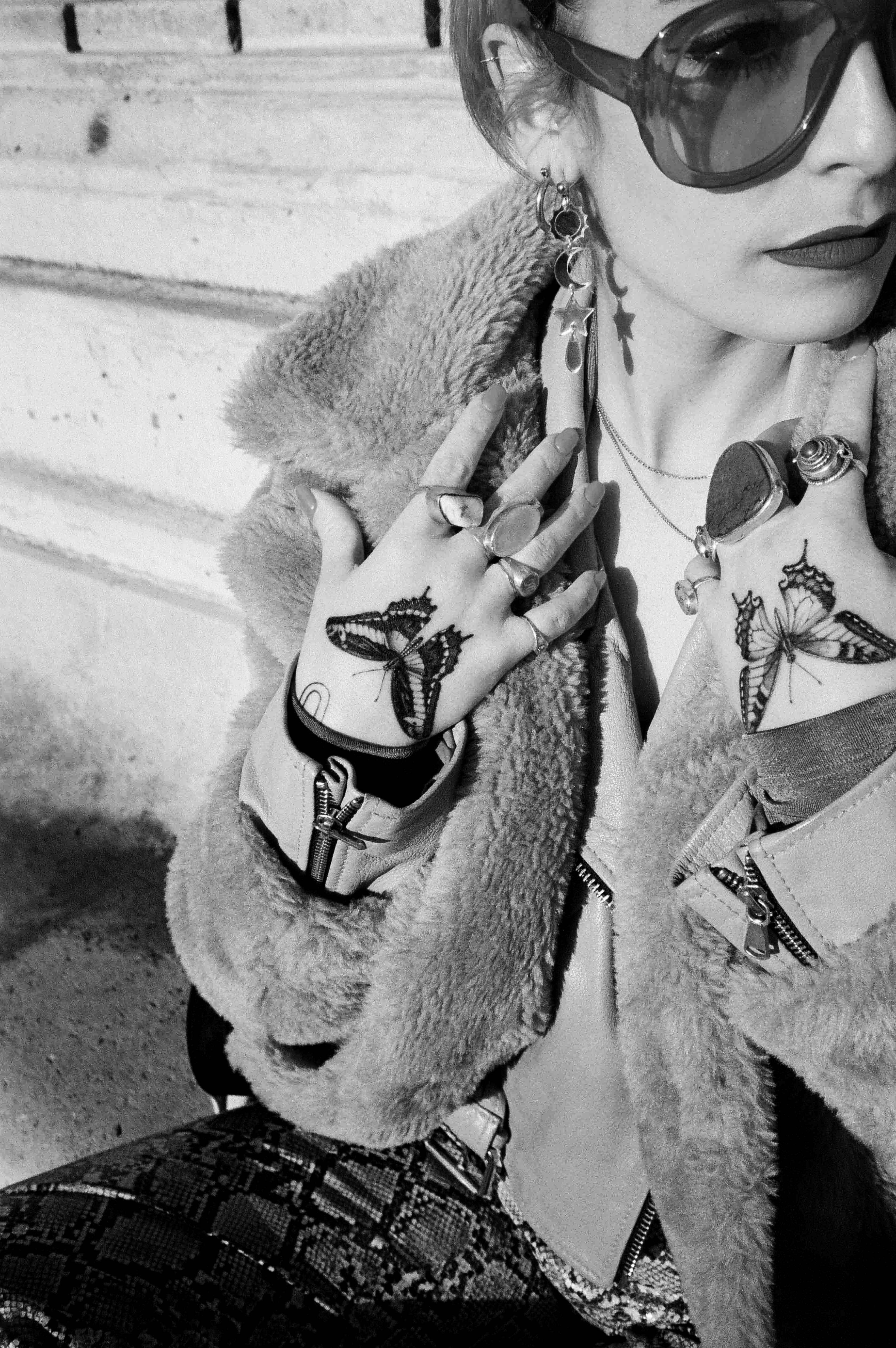 Giovane donna con occhiali da sole, tatuaggi sulle mani e gioielli in un ritratto in bianco e nero, scattato in Piazza Garibaldi a Parma.