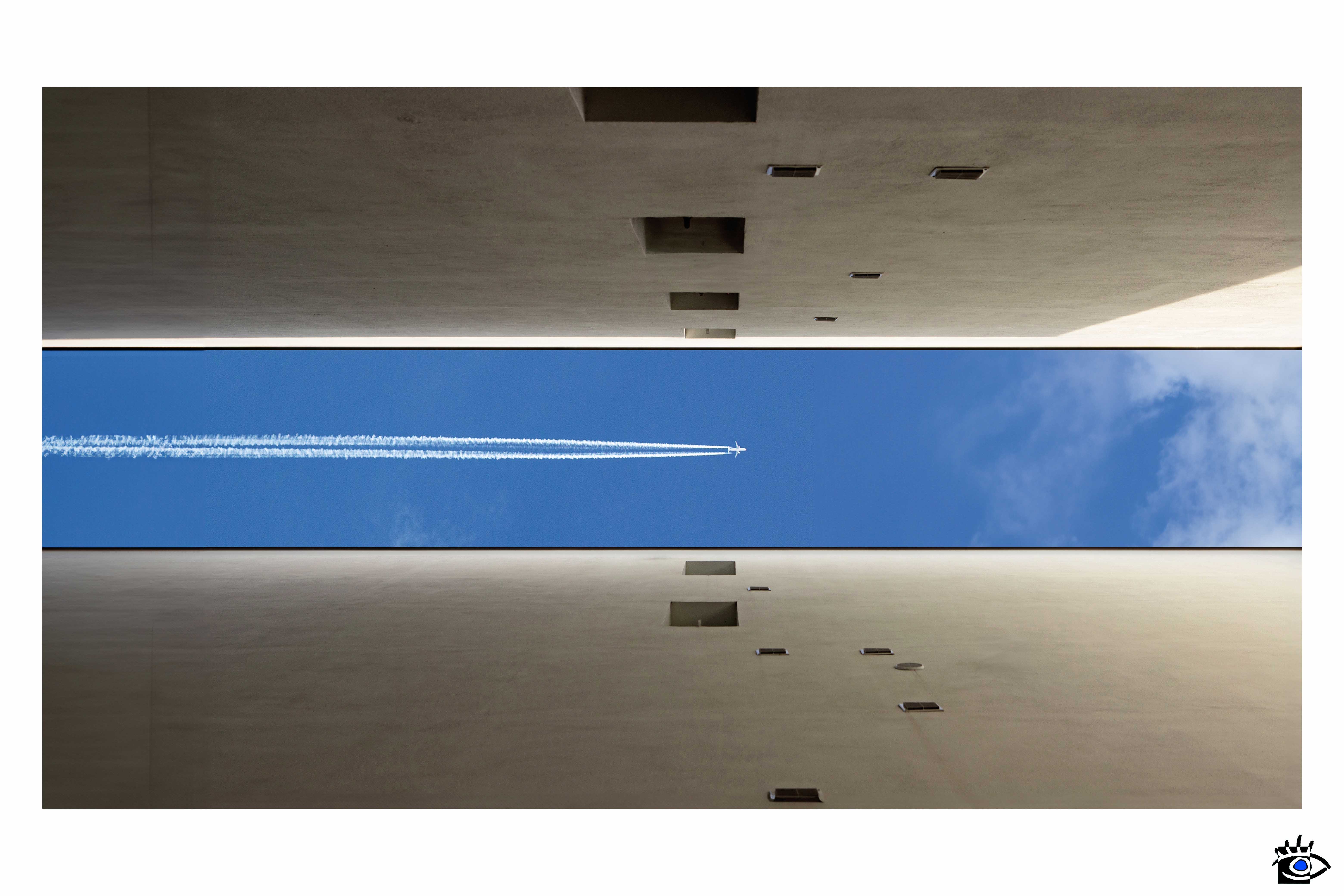 Nella foto, due edifici simmetrici si stagliano contro un cielo sereno, mentre un aereo di linea attraversa il cielo, creando un contrasto dinamico tra la staticità dell'architettura e il movimento della tecnologia moderna
