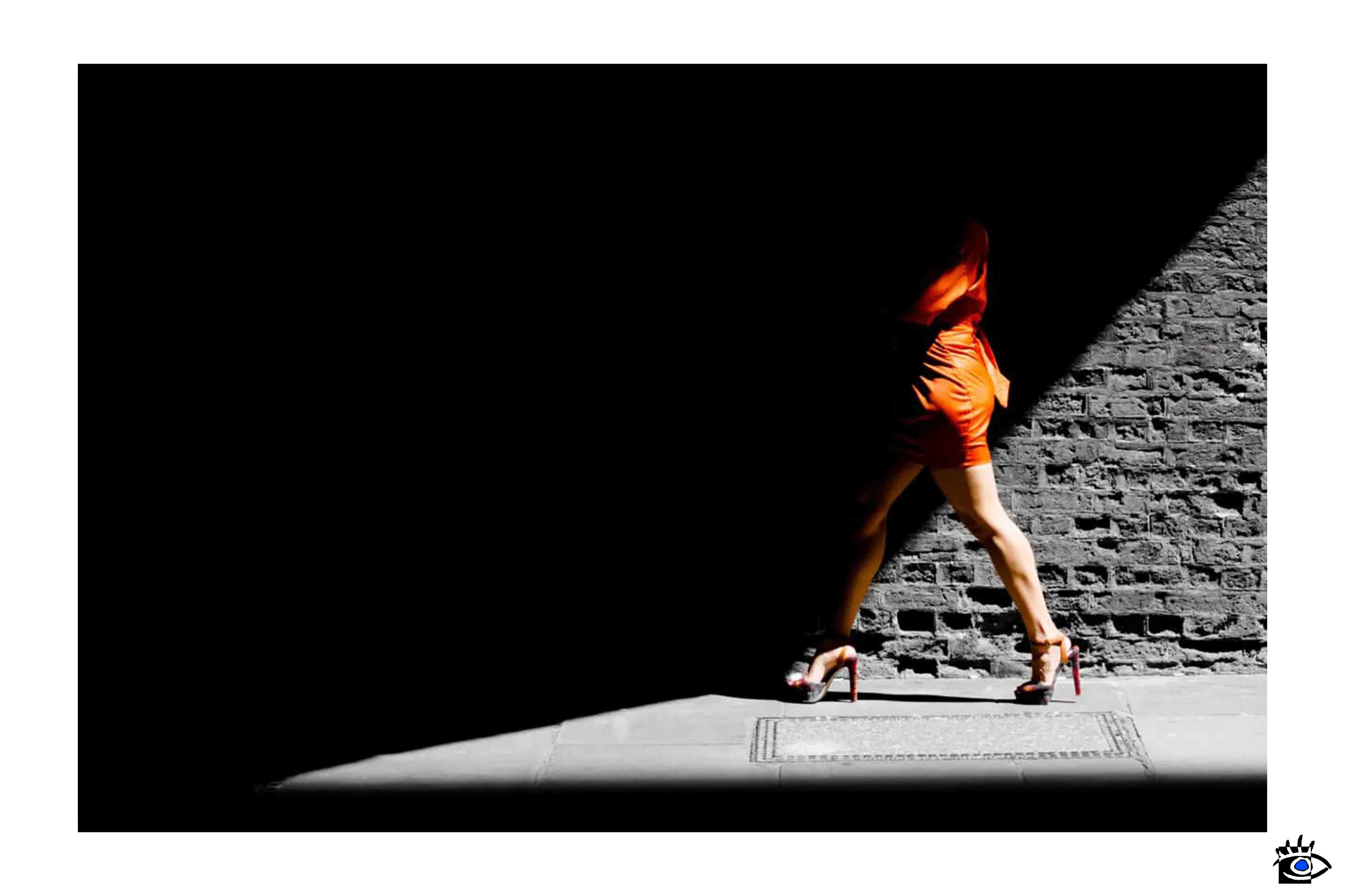 Donna con vestito arancione passa in un vicolo, effetto di linee d'ombra nere aggiunte con Photoshop