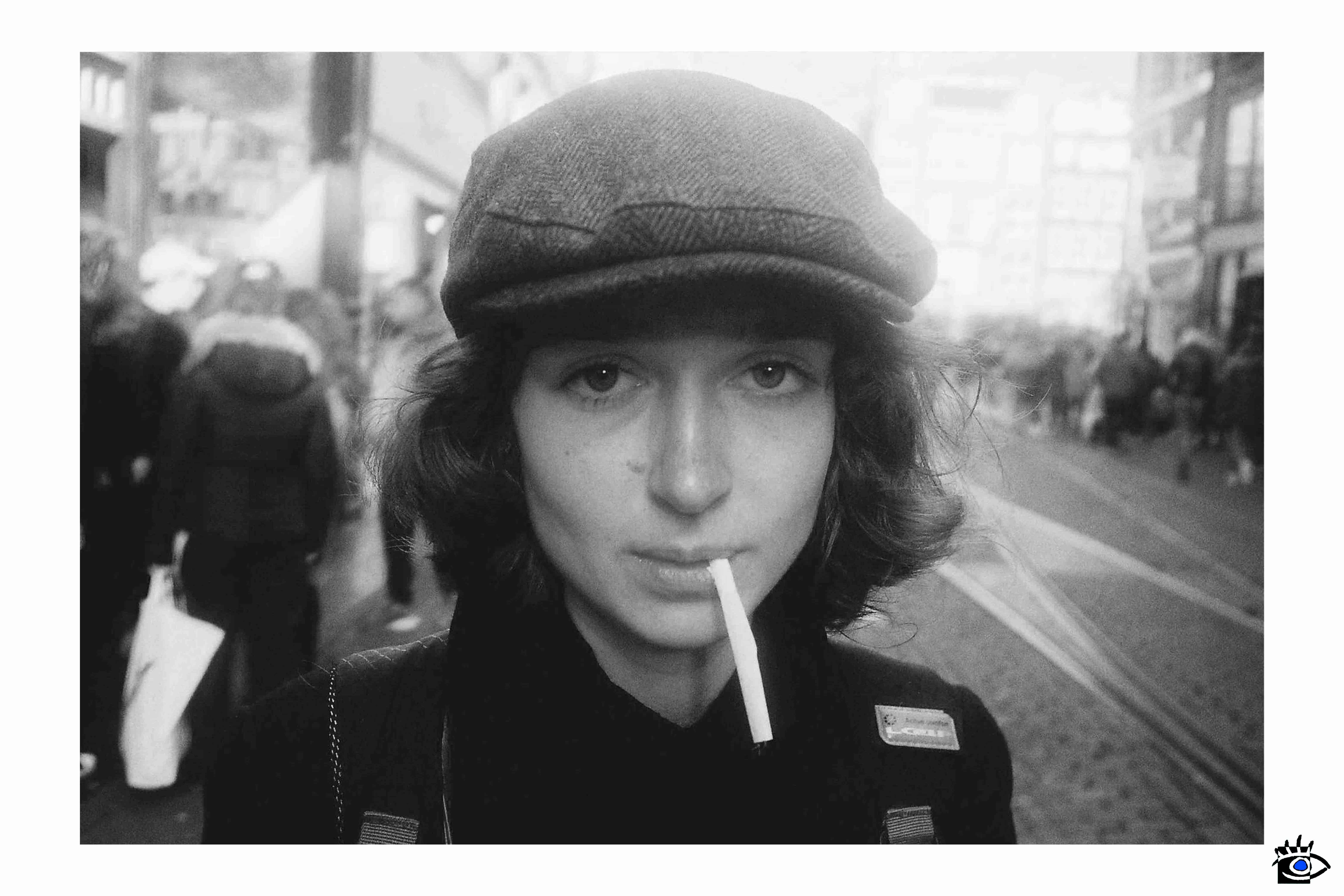 Giovane donna con cappello scozzese e sigaretta, mentre cammina per un vicolo di Lisbona in una giornata autunnale.