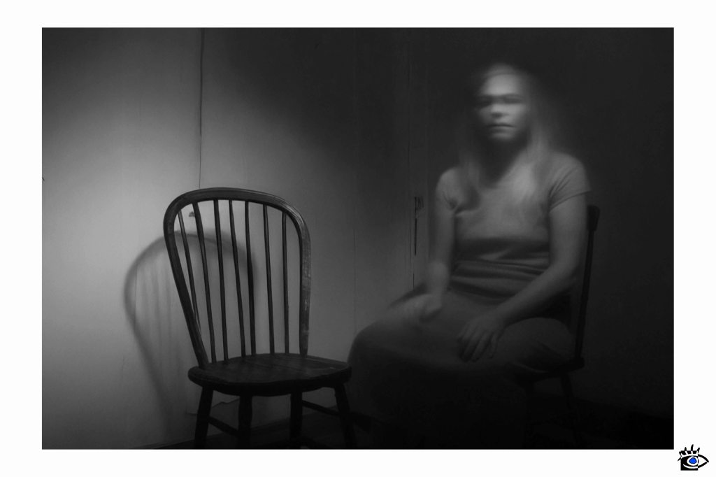 Shadowed figure seated beside empty chair.