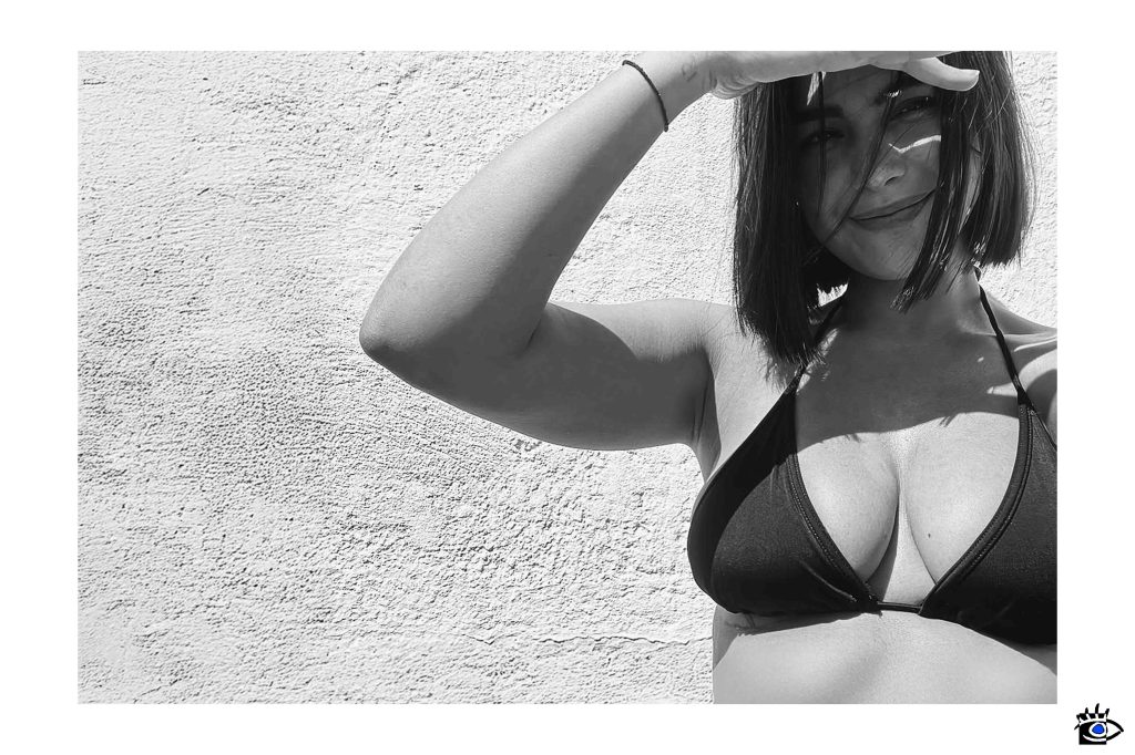 Donna sorridente, bikini nero, luce naturale, muro texturizzato, fotografia in bianco e nero, estate