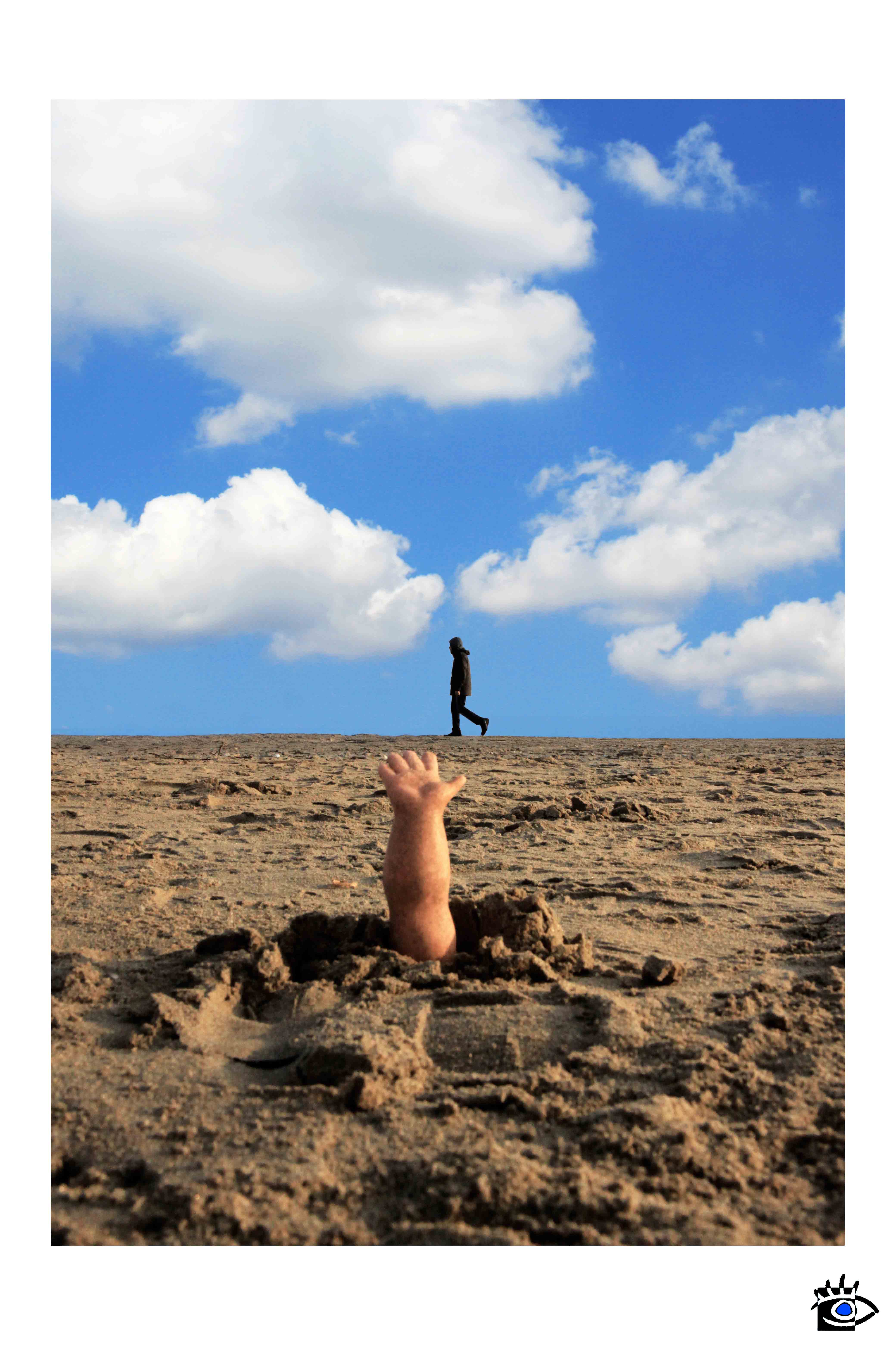 Braccio di una bambola rotta che emerge dalla sabbia mentre una figura solitaria cammina in lontananza sotto un cielo azzurro con nuvole.