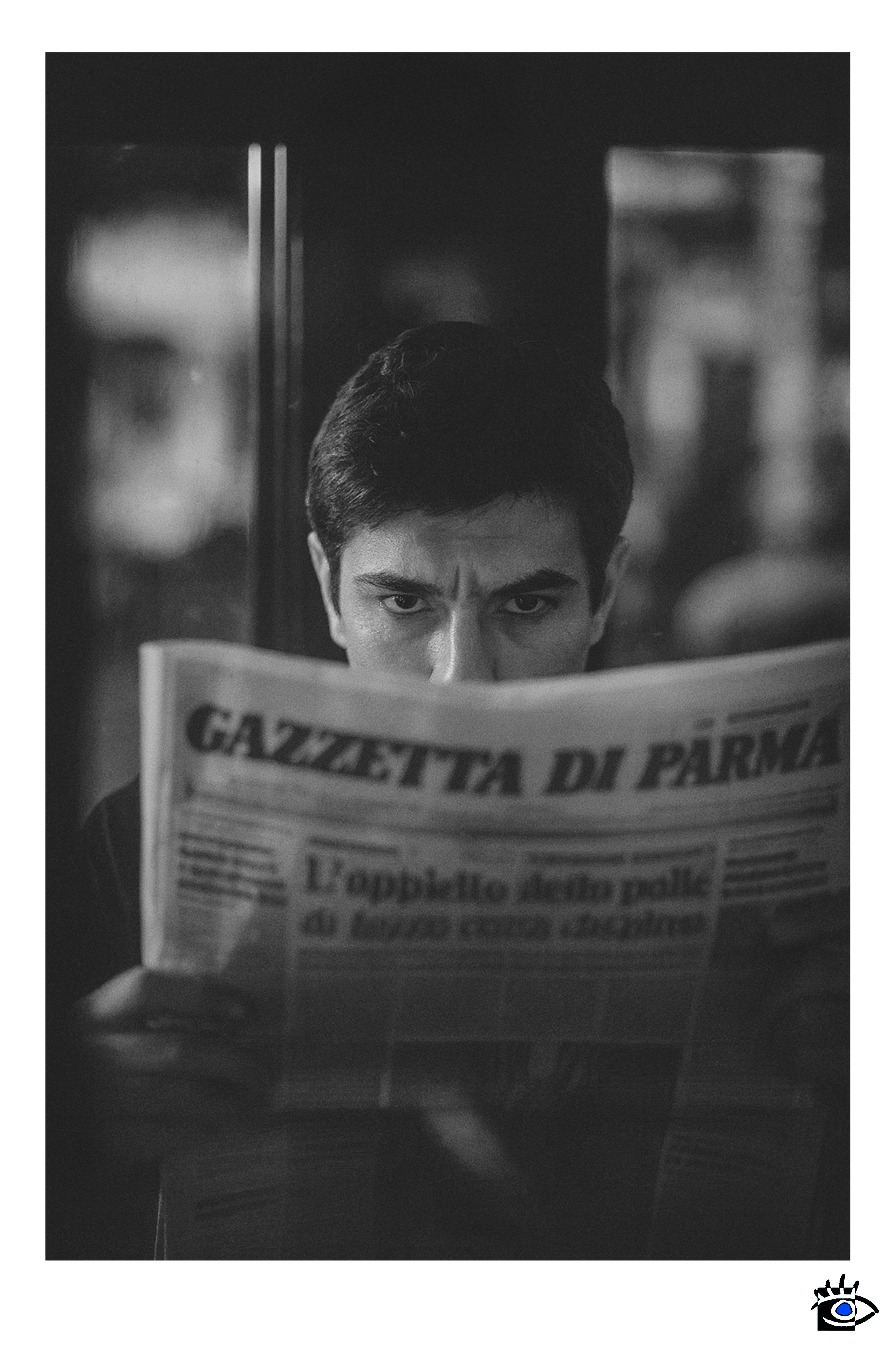 Uomo che legge un quotidiano con espressione intensa, illuminato da una luce calda in un ambiente scuro.