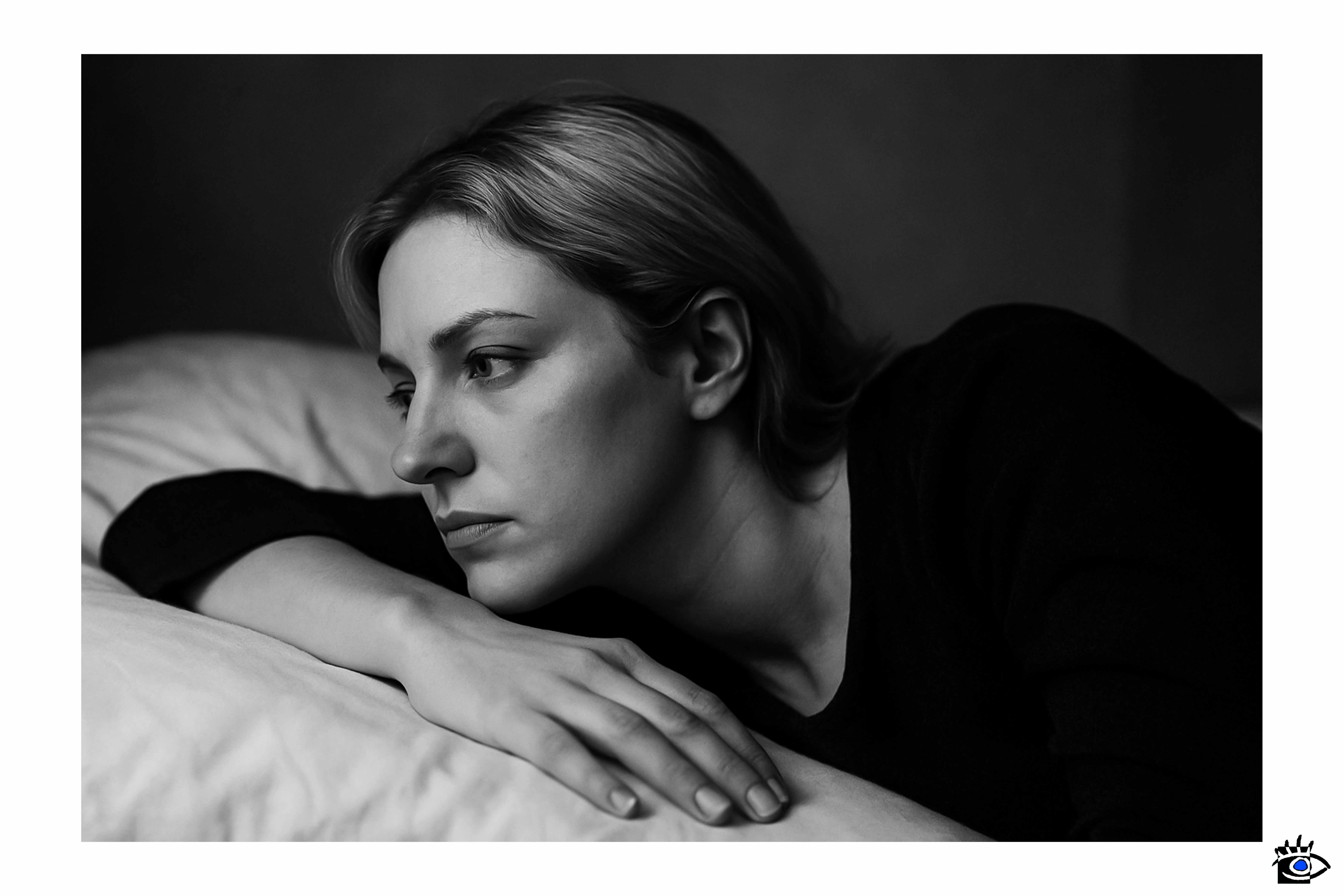 Donna sdraiata su un letto in una stanza, fotografia in bianco e nero, vista di profilo con sguardo rivolto fuori dall’inquadratura.