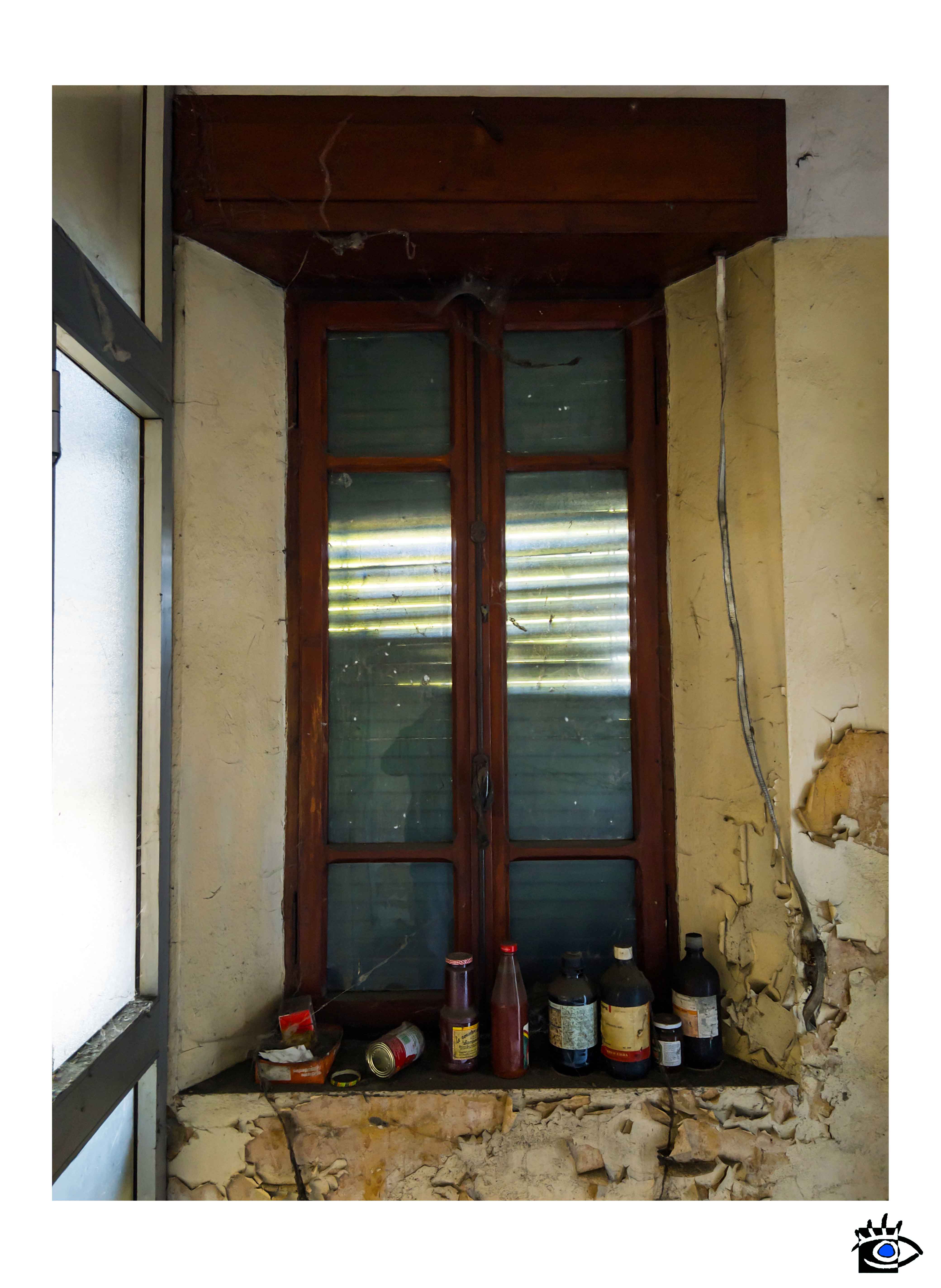 Finestra interna di edificio abbandonato con bottiglie e contenitori lasciati sul davanzale.