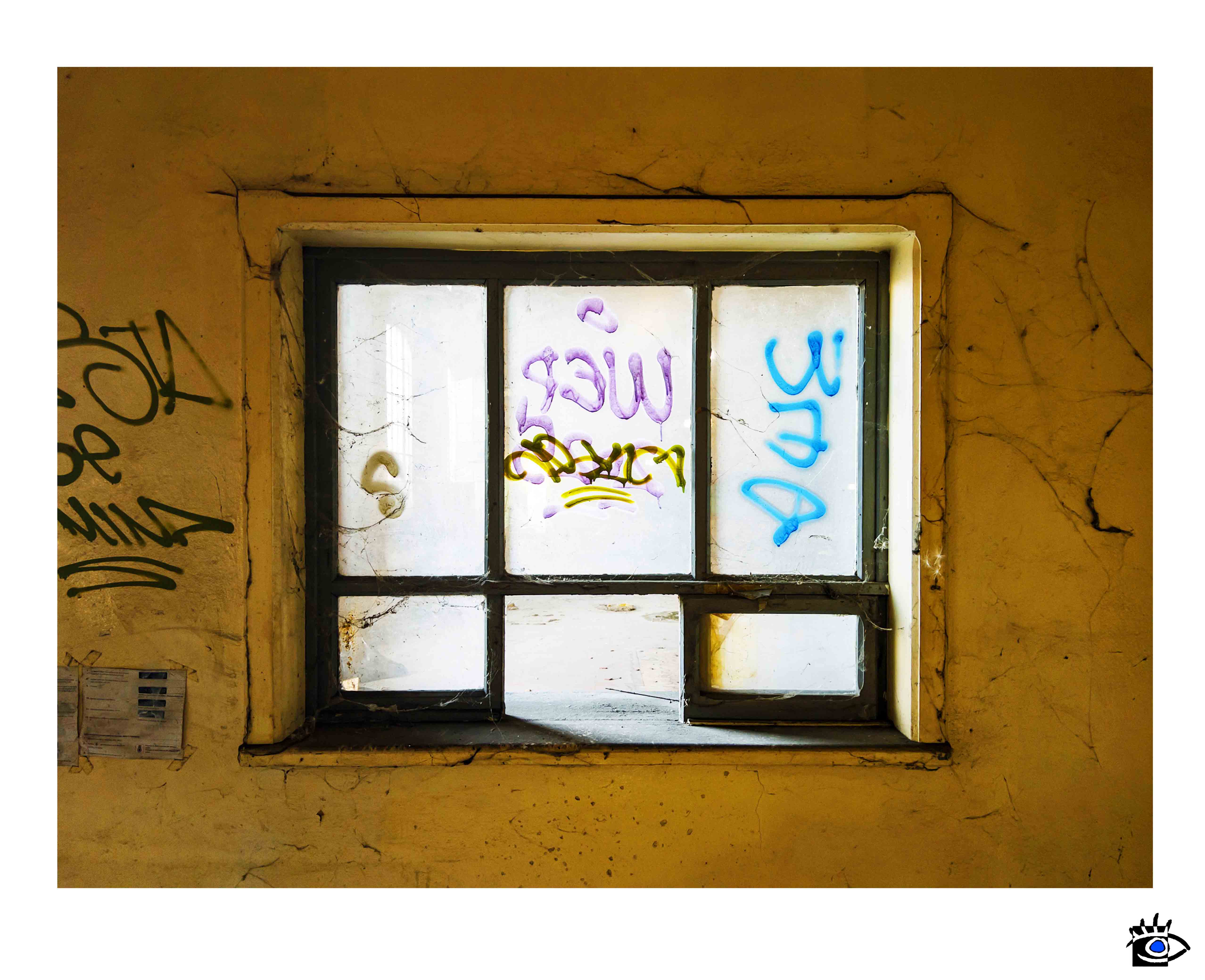 Finestra interna di edificio abbandonato con vetri opachi e graffiti colorati visibili sui pannelli.