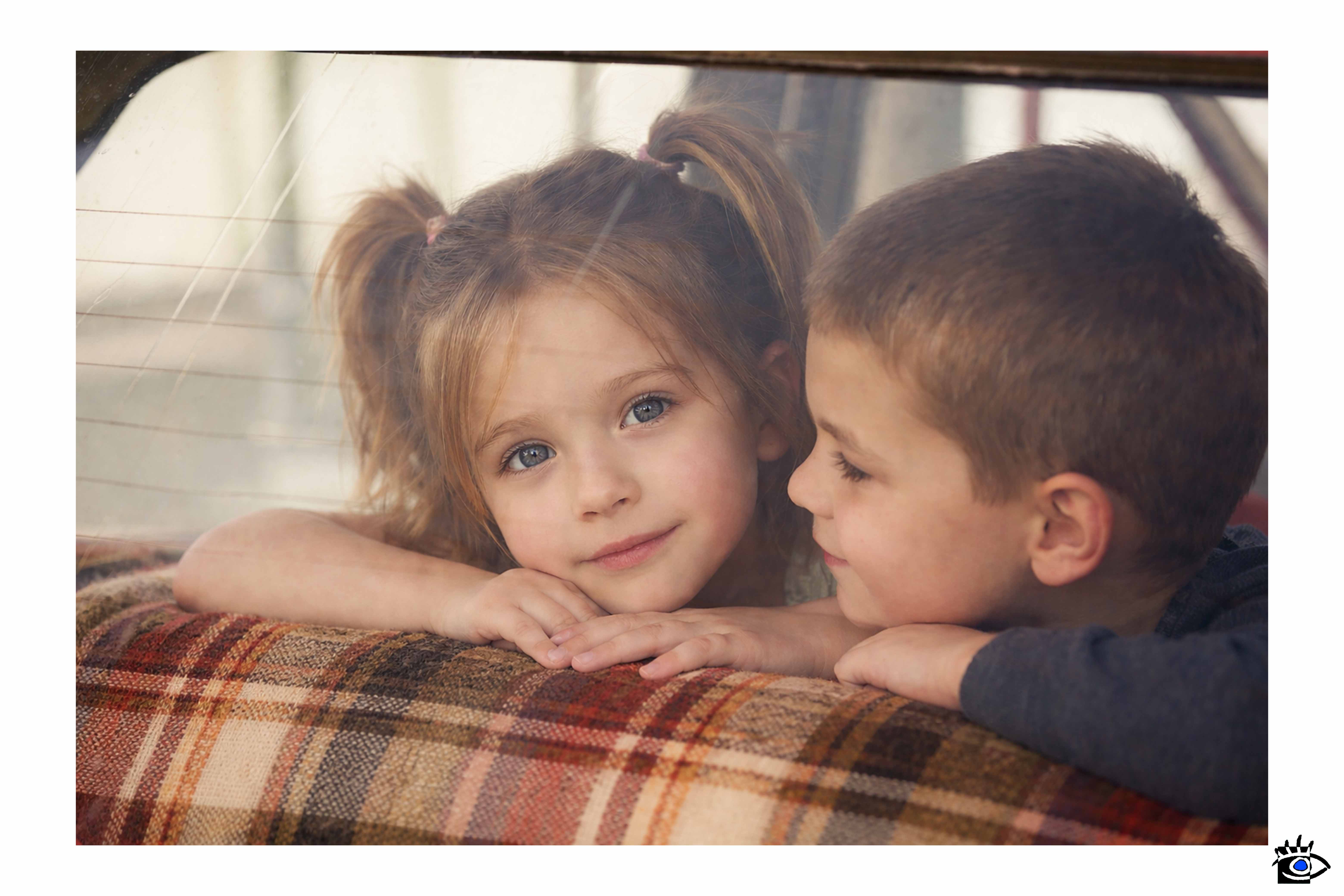 Due bambini seduti sul sedile posteriore di un’auto osservati attraverso il finestrino, uno guarda fuori mentre l’altro è di profilo.